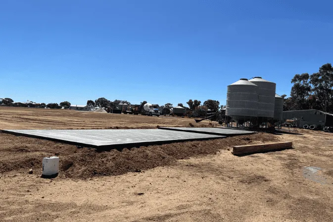 A freshly finished concrete slab on a farm beside grain silos