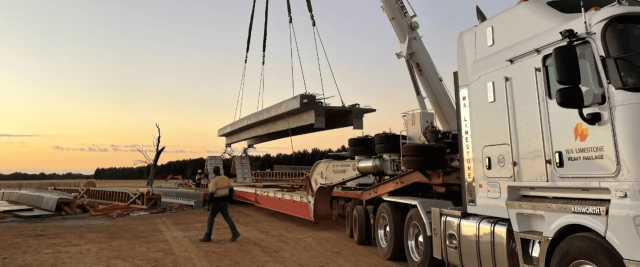 A crane lifting a precast bridge beam from a truck on site