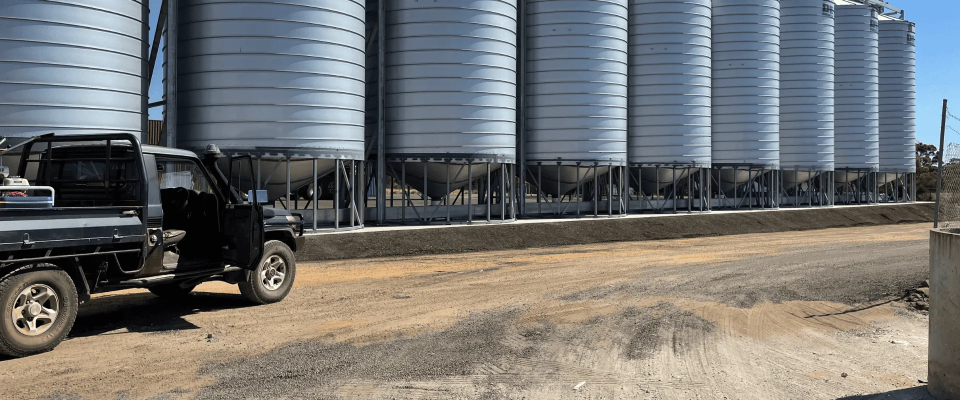 A row of grain silos on a concrete pad with a ute parked in front